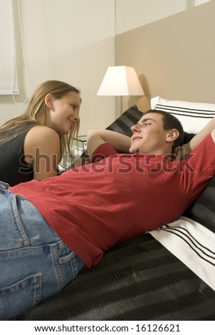 Man and woman relax on bed talking to each other. Vertically framed photo.