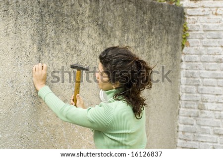 Woman holds hammer and nail. She is nailing into wall. Horizontally framed photo.