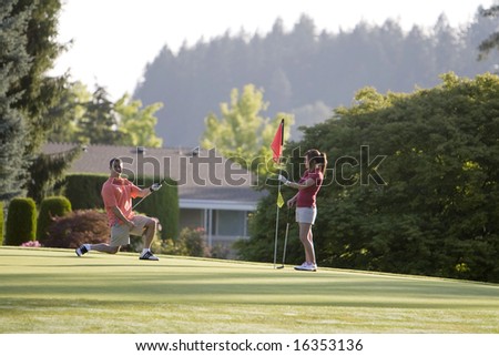 Couple playing golf by a golf cart. Horizontally framed shot.