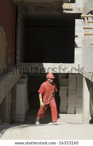 Construction worker walks across job site. He is wearing orange suit and hard hat. Vertically frame photo.