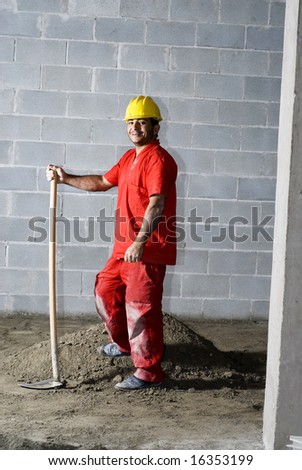 Construction worker stands next to dirt pile holding a ho. He is smiling at the camera. Vertically framed photo.