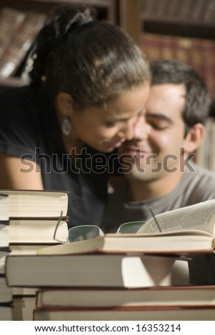 Woman sits on man\'s lap. There are books on the table and in the background. Vertically framed photo.