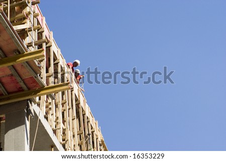 Construction workers lean over edge of new building while pulling equipment up with rope. Horizontally framed photo.