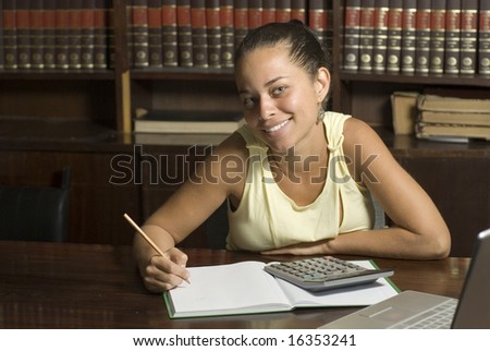 Woman studies in library. She is smiling and looking at the camera. Horizontally framed photo.