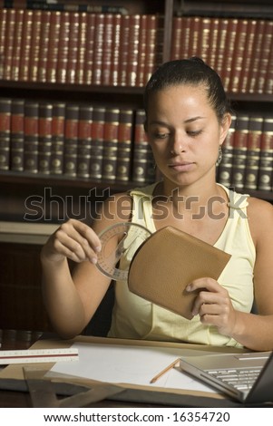 Woman seated in library puts a protractor away in its case. There are books behind her and she is seated at a table. Vertically framed photo.