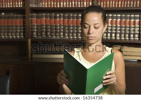 Woman sits in library holding and reading book. Horizontally framed photo.