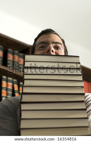 Man with glasses carries a stack of books through a library. Vertically framed photo.