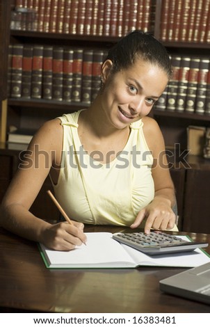 Woman studies in library with notebook, calculator and laptop. Vertically framed photo.