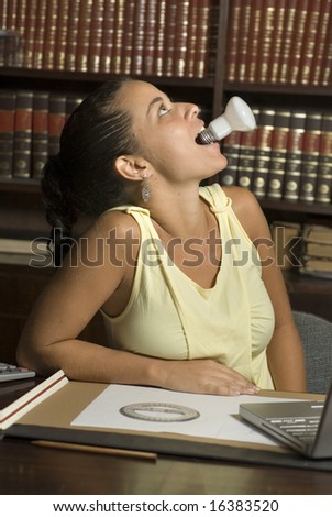 Woman plays in library by holding a light bulb in her mouth. Photo is taken from the side. Vertically framed photo.