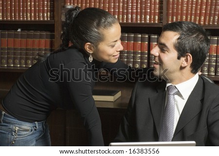 Man and woman sit in library. Woman leans over man who is wearing suit. Horizontally framed photo.