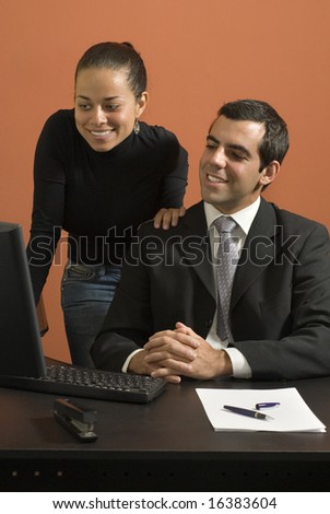 Businessman and woman at desk looking at a computer. They are both smiling. Vertically framed photo
