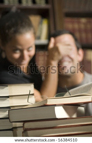 Woman covers man\'s eyes while studying in library. Vertically framed photo.