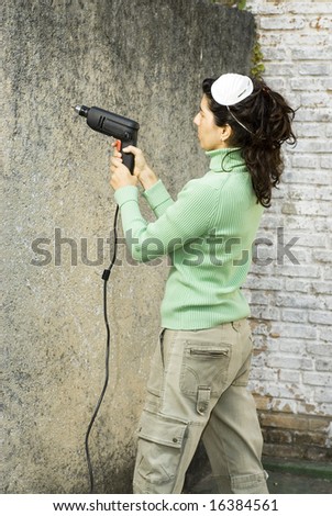 Woman drills hole in wall. She is wearing a dust mask on her head. Vertically framed photo.