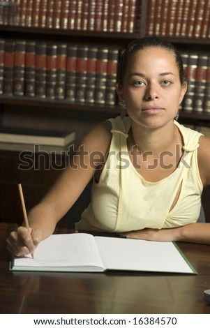 Woman sits at a table in the library. She is studying and writing in a notebook.  Vertically framed photo.