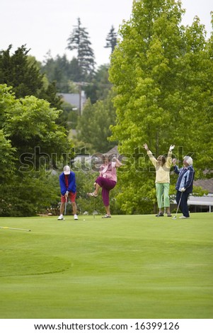 Group of four women celebrating with their arms up while playing golf. Vertically framed photo.