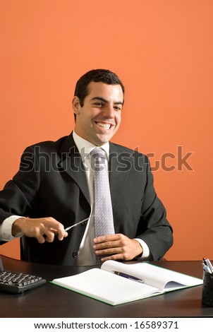 Smiling businessman seated at his computer pretending to cut his tie with scissors. Vertically framed photo.