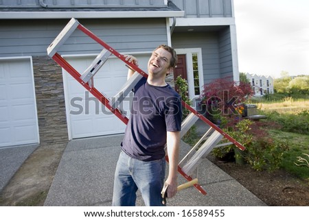 Laughing man standing in front of house holding ladder and hammer. Horizontally framed photo.