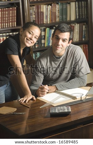 Young, smiling couple study together in an office with many books and a computer. Horizontally framed photo.