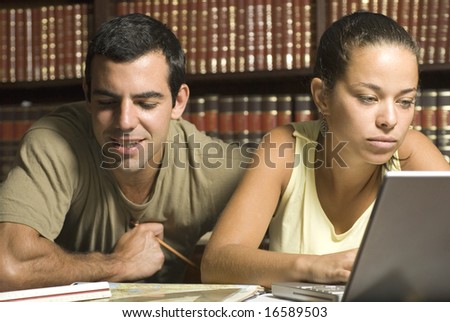 Young couple study together in an office with many books and a computer. Horizontally framed photo.