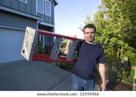 Smiling man standing in front of house holding ladder and hammer. Horizontally framed photo.