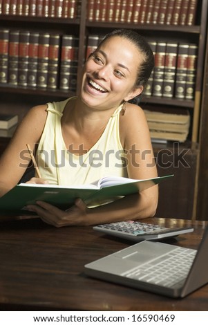 Woman laughing while she reads a book in a library. Vertically framed photo.