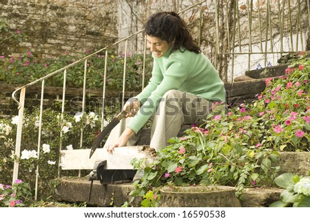 Woman sitting on stairs holds a board in a vice. She is smiling and sawing the board. Horizontally framed photo.