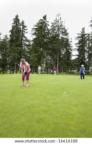 Elderly woman teeing off on the golf course as her three friends watch. Vertically framed photo.