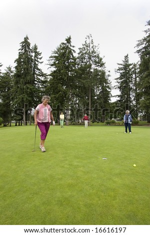 Elderly woman going after her golf ball on the golf course as her three friends watch. Vertically framed photo.