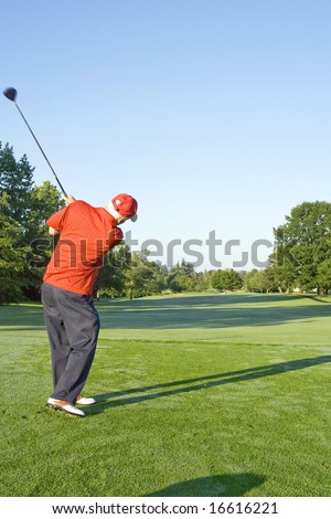 Man following through his golf swing with the ball frozen against the blue sky. Vertically framed photo. (2nd in a series)