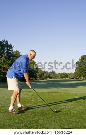 Man lines up his golf club with a golf ball. Vertically framed photo.