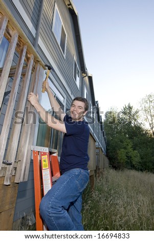 Smiling man on ladder hammering a porch. Vertically framed photo.