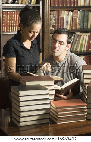 Students Working with stacks of books in front of them, and books in the background. Vertically framed photo.