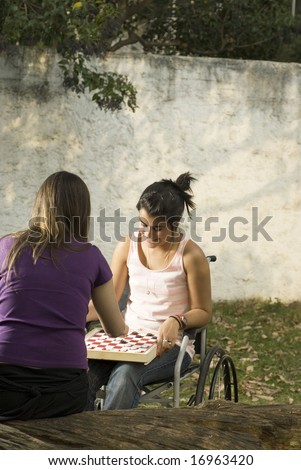 Young girl in wheelchair playing cards in with another girl. Vertically framed photo.
