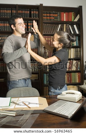 Two students giving each other high fives in a library. Vertically framed photo.
