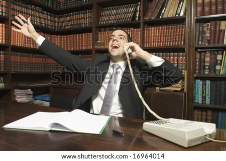 Businessman on phone is jubilant with his arms up in the air. Horizontally framed photo.
