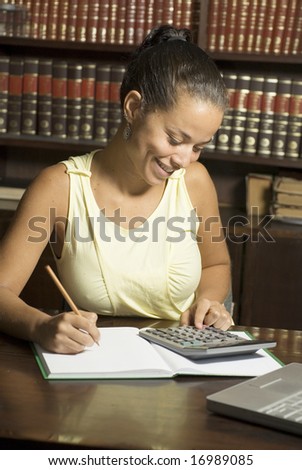 Smiling woman seated at desk with paper, pencil, and calculator. Vertically framed photo.