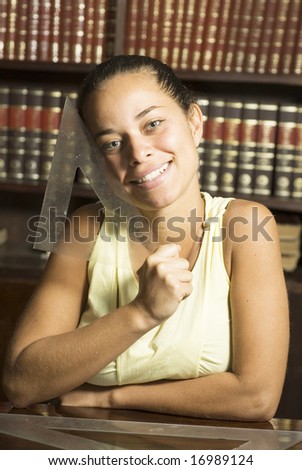 Smiling girl holding a drafting tool in an office full of books. Vertically framed photo.