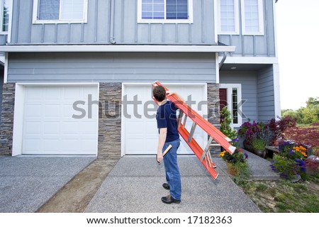 Man standing in front of house holding ladder and hammer. Horizontally framed photo.
