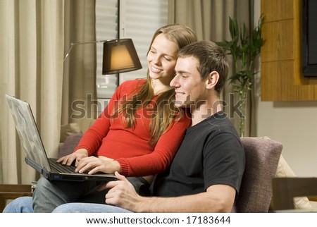 Young smiling, couple at home working on a laptop computer. Horizontally framed photo.