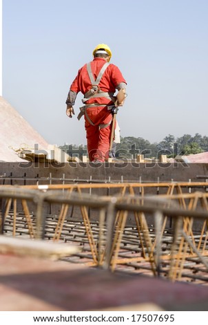 The worker is standing on top of the unfinished structure.  He is walking away from the camera.  Vertically framed shot.