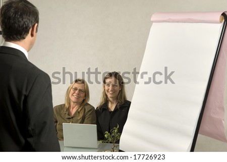 A Boss in instructing his employees in a business meeting.  The two girls are smiling at him.  Horizontally framed shot.