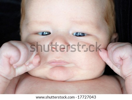 A young baby is posing in a studio.  He is looking down and away from the camera.  Horizontally framed shot.