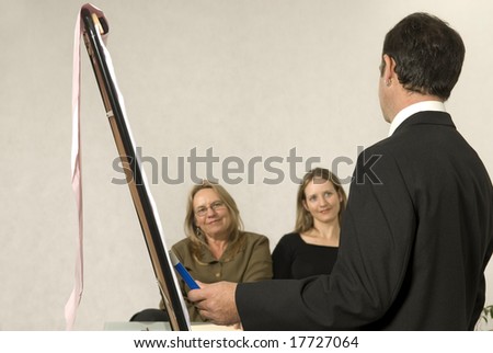 A Boss in instructing his employees in a business meeting.  The two girls are smiling at him.  Horizontally framed shot.
