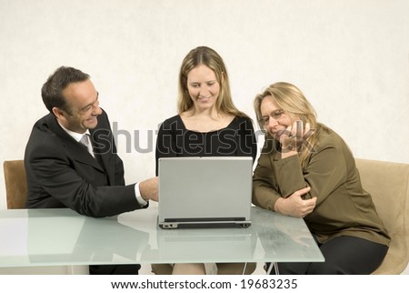 Three people are in a business meeting together.  They are smiling and looking at the screen of the laptop in front of the younger woman.  Horizontally framed shot.
