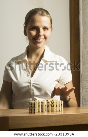 Smiling young woman seated at desk playing dominoes. Vertically framed photo.