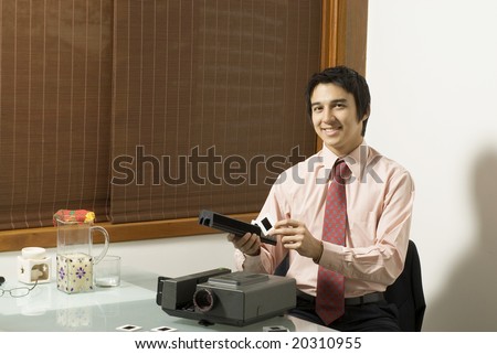 Man smiling as he puts slides in a slide show projector. Horizontally framed photo.