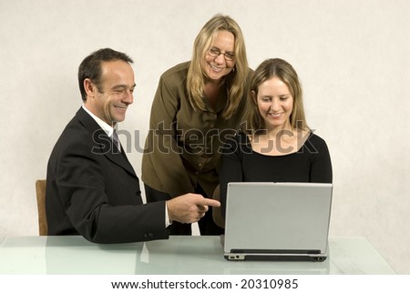 Three people are in a business meeting.  They are smiling and looking at the screen of the laptop.  Horizontally framed shot.