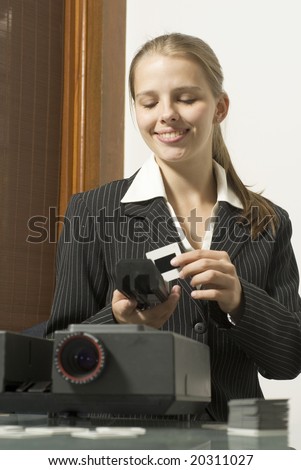 Woman  smiling as she places slides in  a slide show projector. Vertically framed photo.