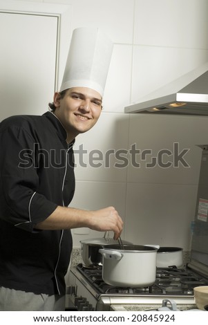 Smiling chef standing over a stove stirring the contents from a pot on the stove. Vertically framed photo.