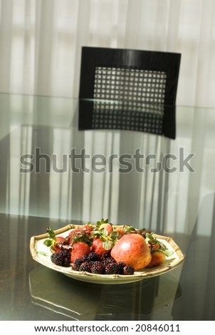 Fruit plate with raspberries, blackberries, strawberries, and an apple on it on a table. Vertically framed photo.